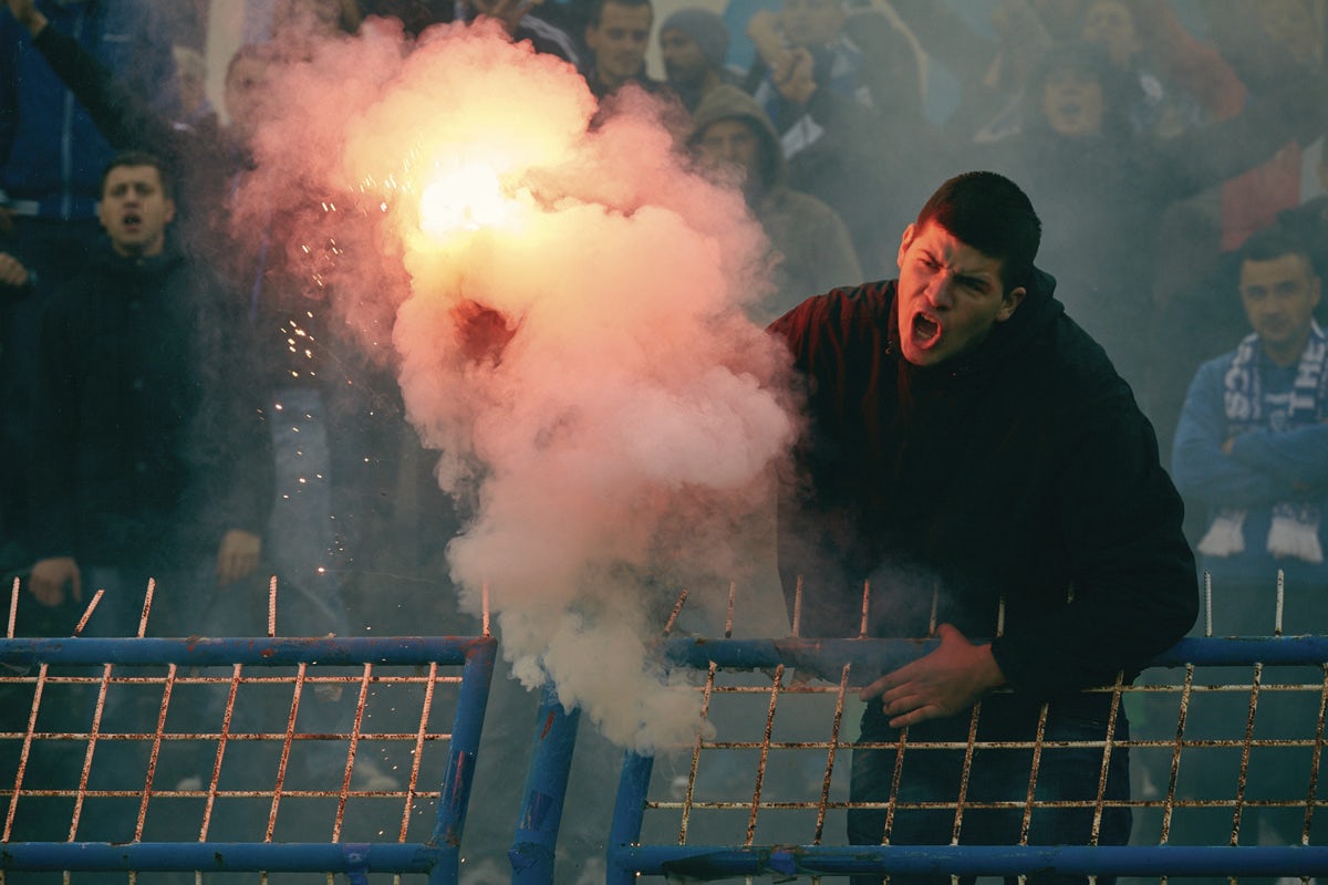 A fan holds a flare at a FK Zeljeznicar Sarajevo vs FK Sarajevo match. Photo by Robin Bharaj for Copa90. 