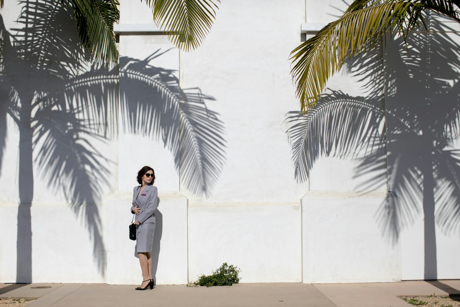 Actor playing Diana Markosian mother stood by a wall under palm trees 