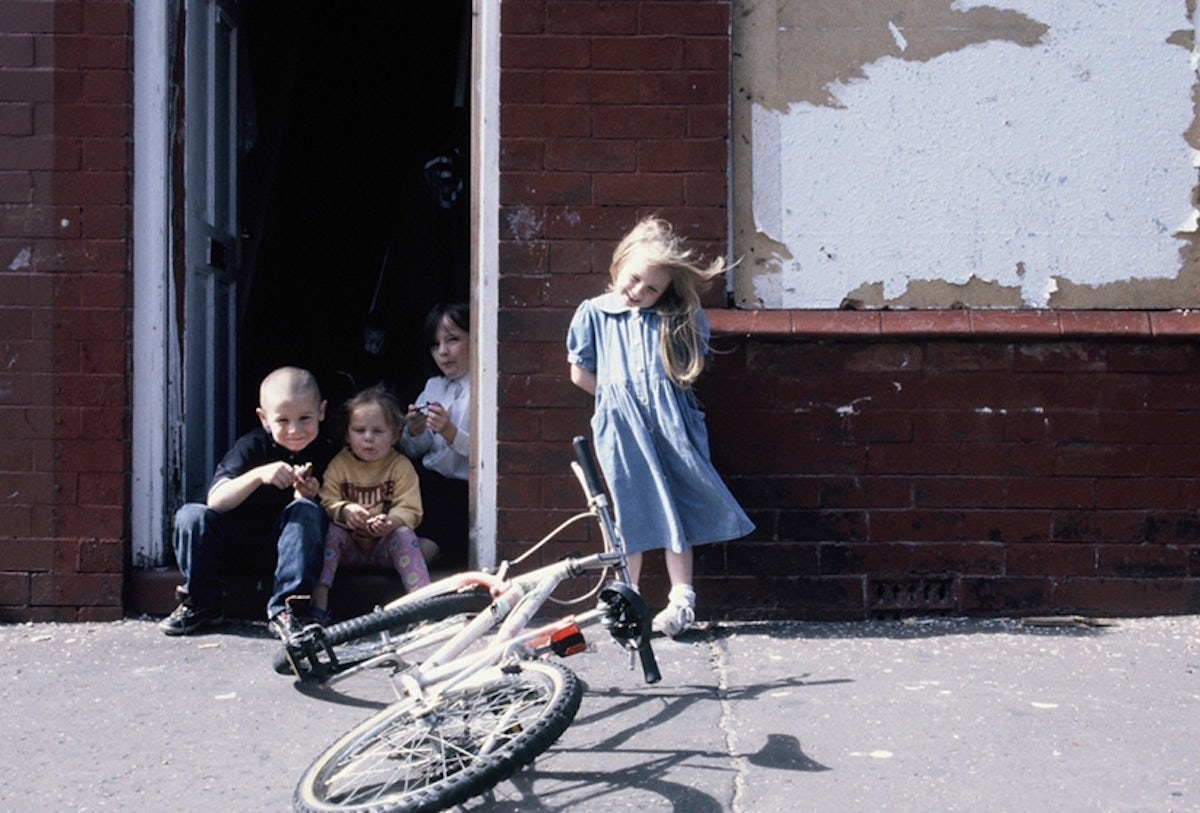 Street photograph by Anne Worthington showing children sat in a doorway next to a bicycle