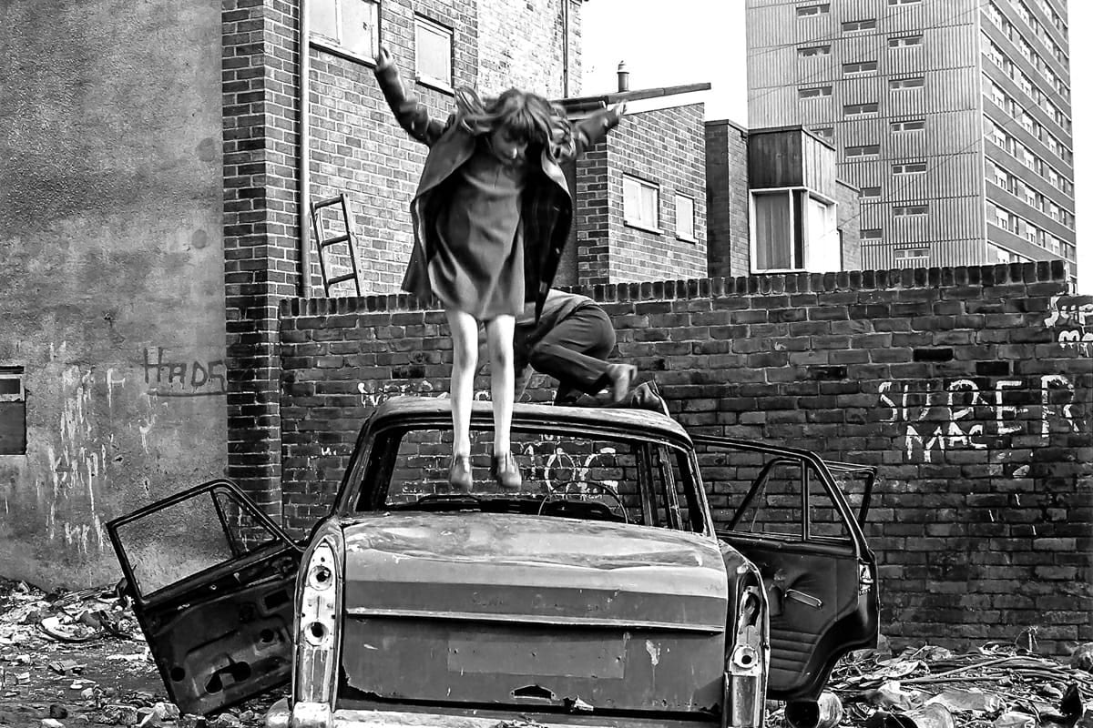 Black and white photograph by Tish Murtha of a child jumping on an old car