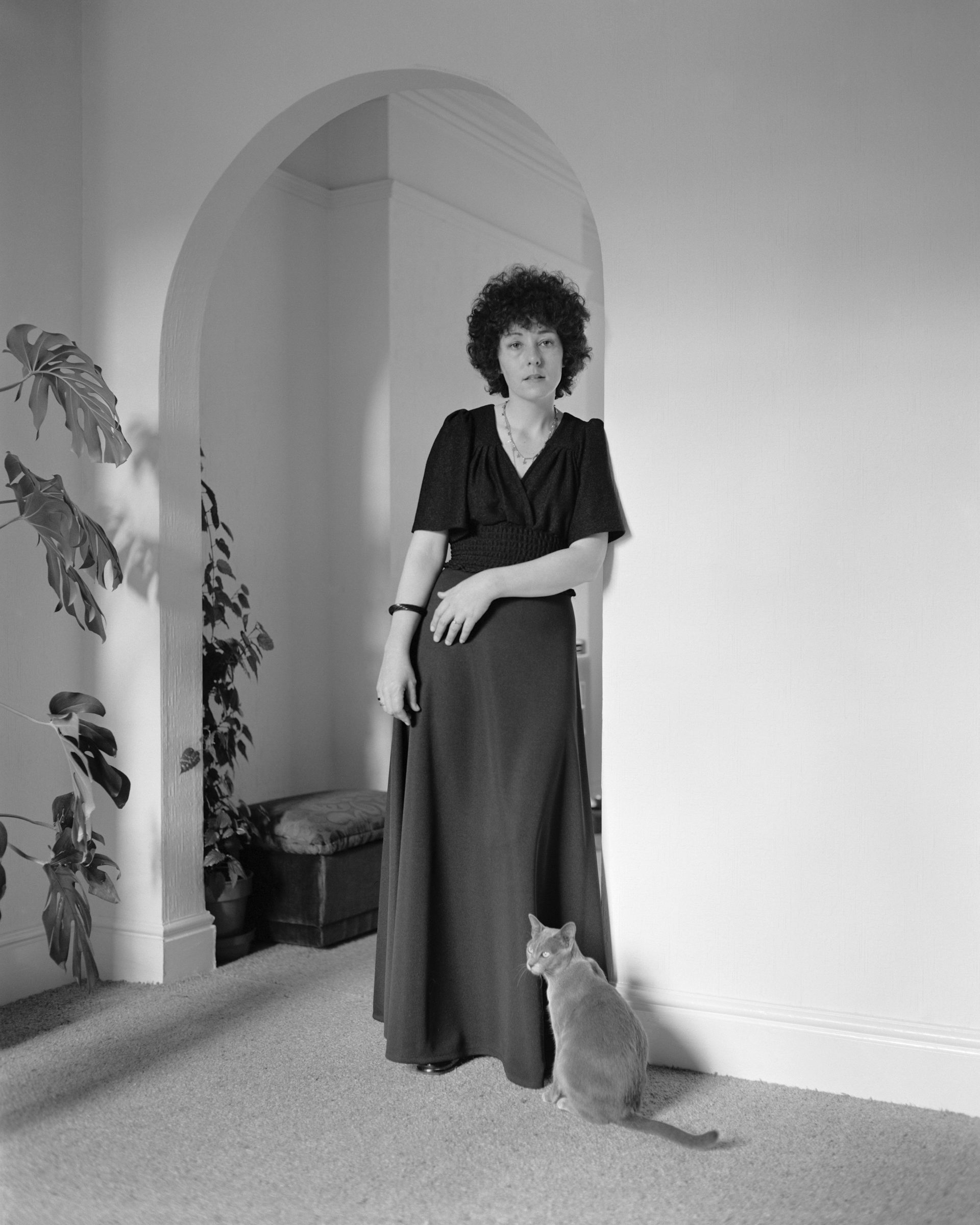 Black and white photograph of a woman in a long dress next to a cat, which features in Life As It Is by John Myers