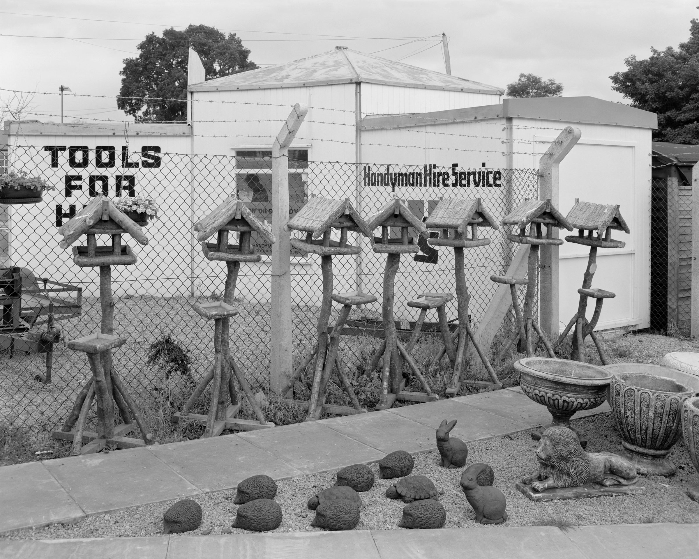 Black and white photograph of an outdoor garden store selling bird rables and ornaments, which features in Life As It Is by John Myers