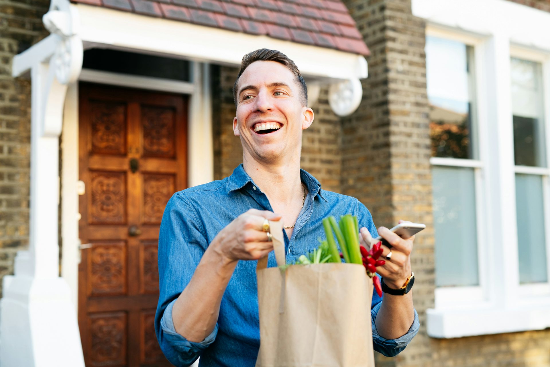 Photograph of a person outside a house carrying a paper bag with produce