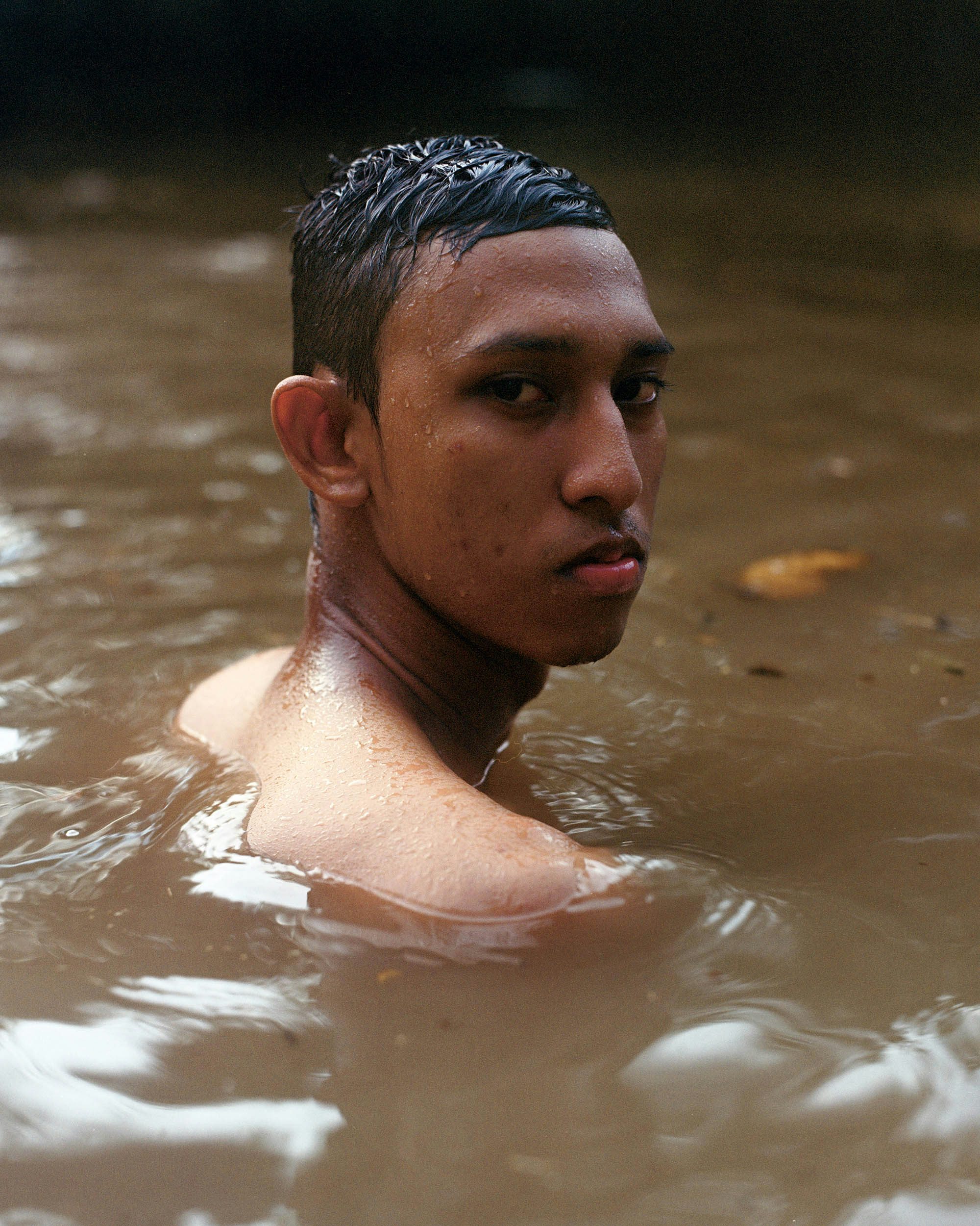 Portrait photograph of a person in a river looking back towards the camera