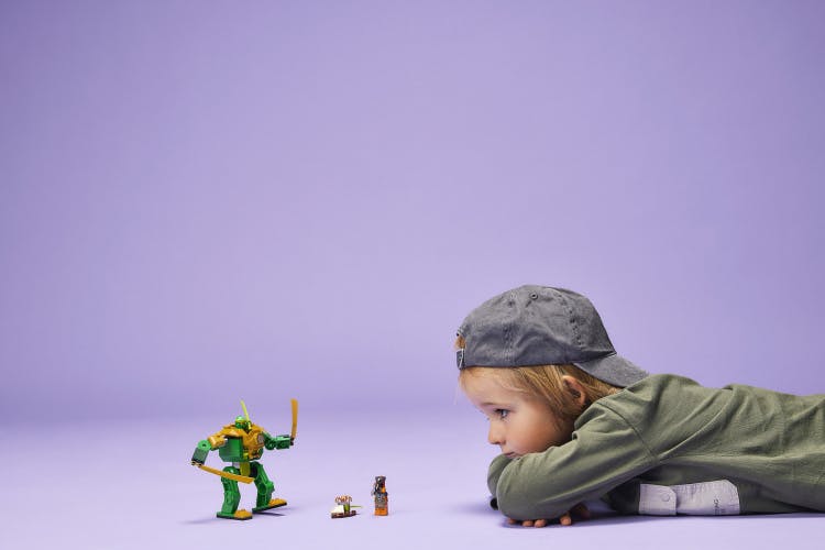 Photograph of a child lying on the ground facing a Lego Ninja figuring