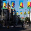 Photograph of Morag Myerscough's installation on Oxford Street, featuring colourful flags that read 'Clean' in the foreground and 'Power' in the background