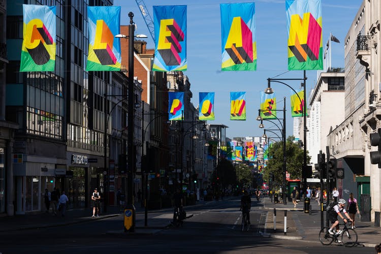 Photograph of Morag Myerscough's installation on Oxford Street, featuring colourful flags that read 'Clean' in the foreground and 'Power' in the background
