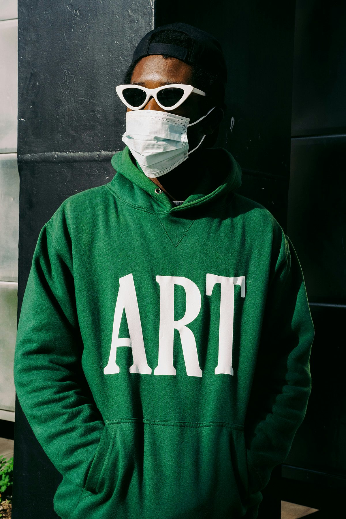 Portrait photograph of a person wearing sunglasses, a mask, and a green hoodie feauturing the word 'Art' by Jeremiah Babatunde