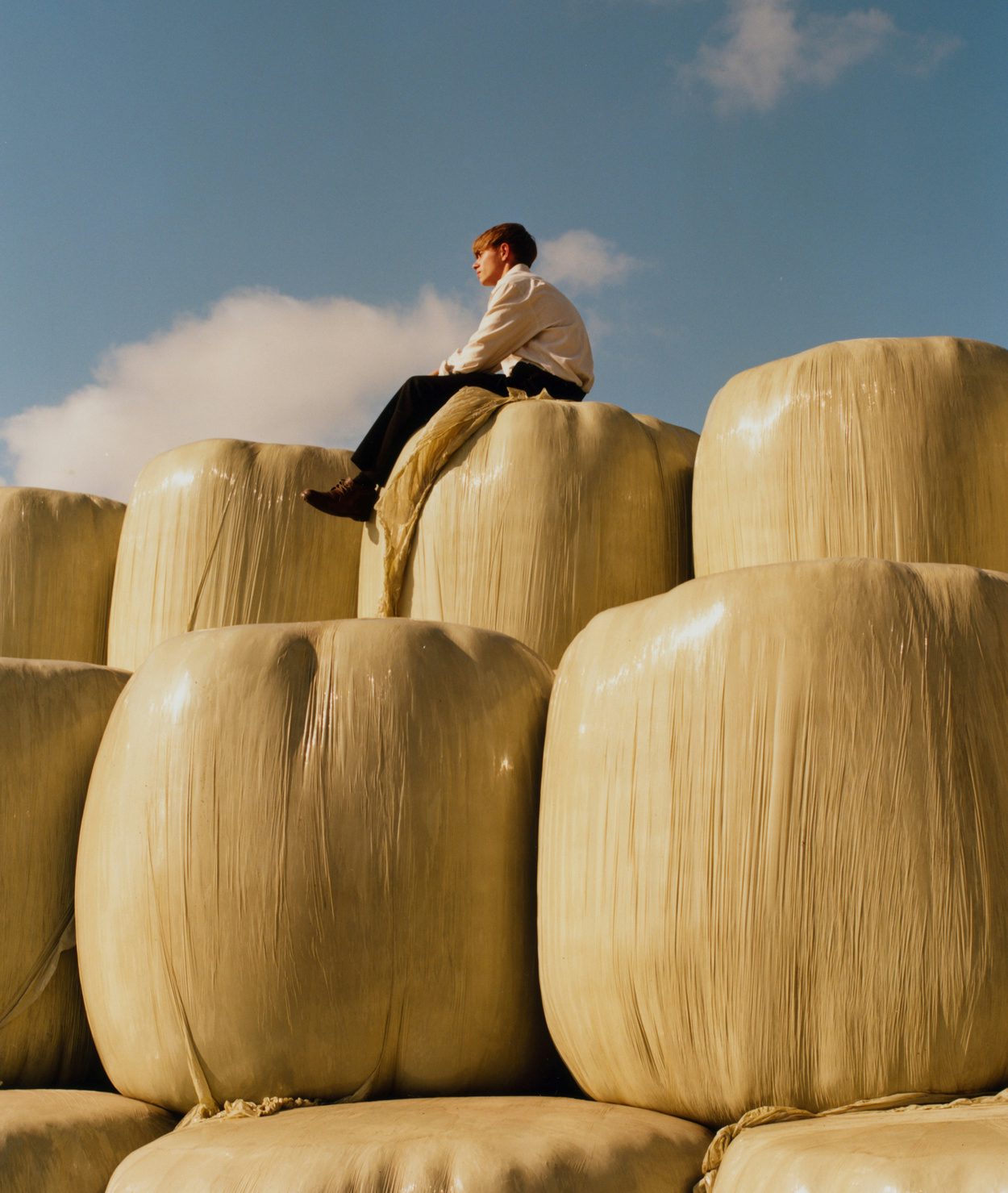 Photograph by Niall Hodson of a person sat on top of stacks of hay bales