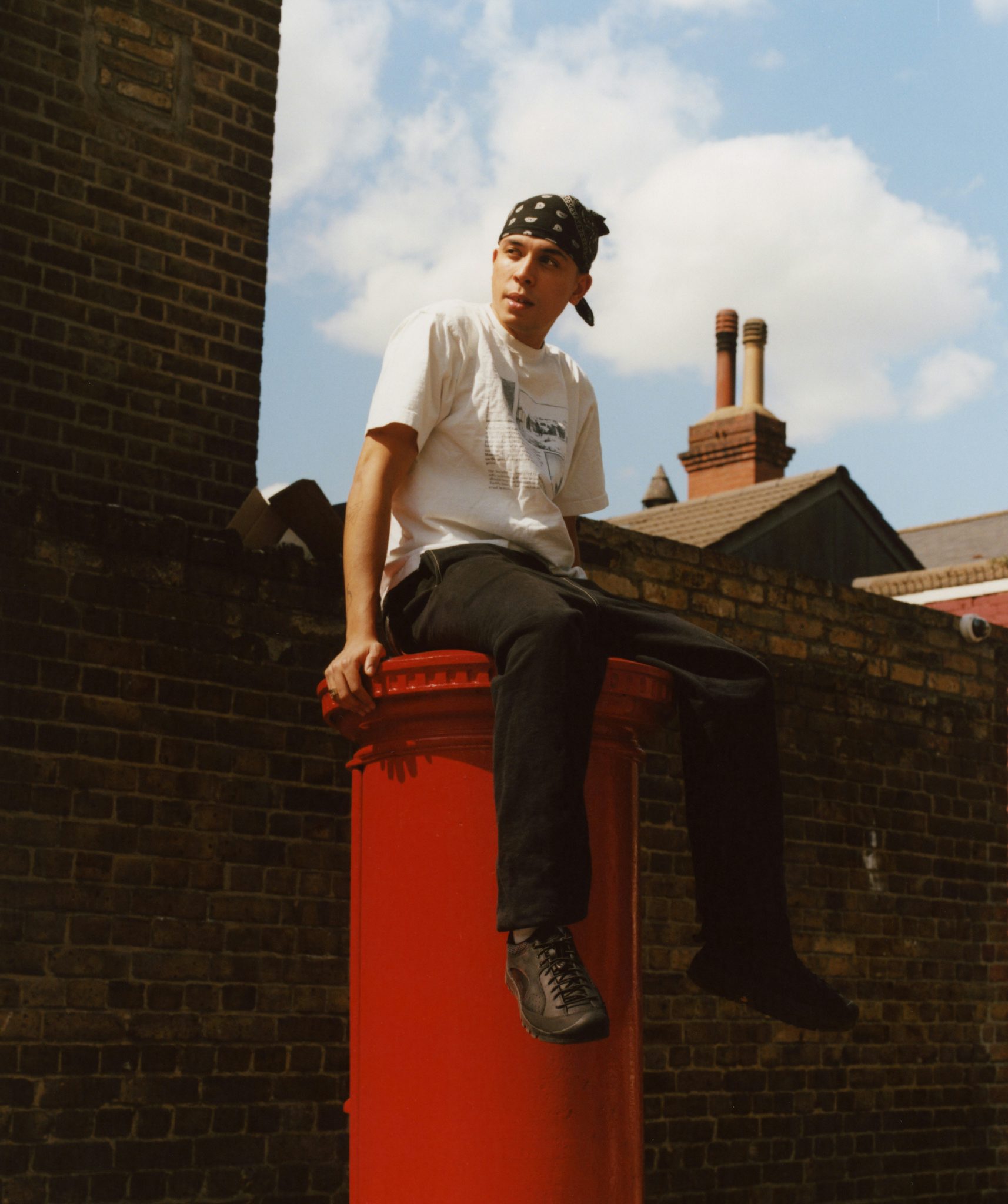 Photograph by Niall Hodson of a young person in a bandana sat on top of a red post box