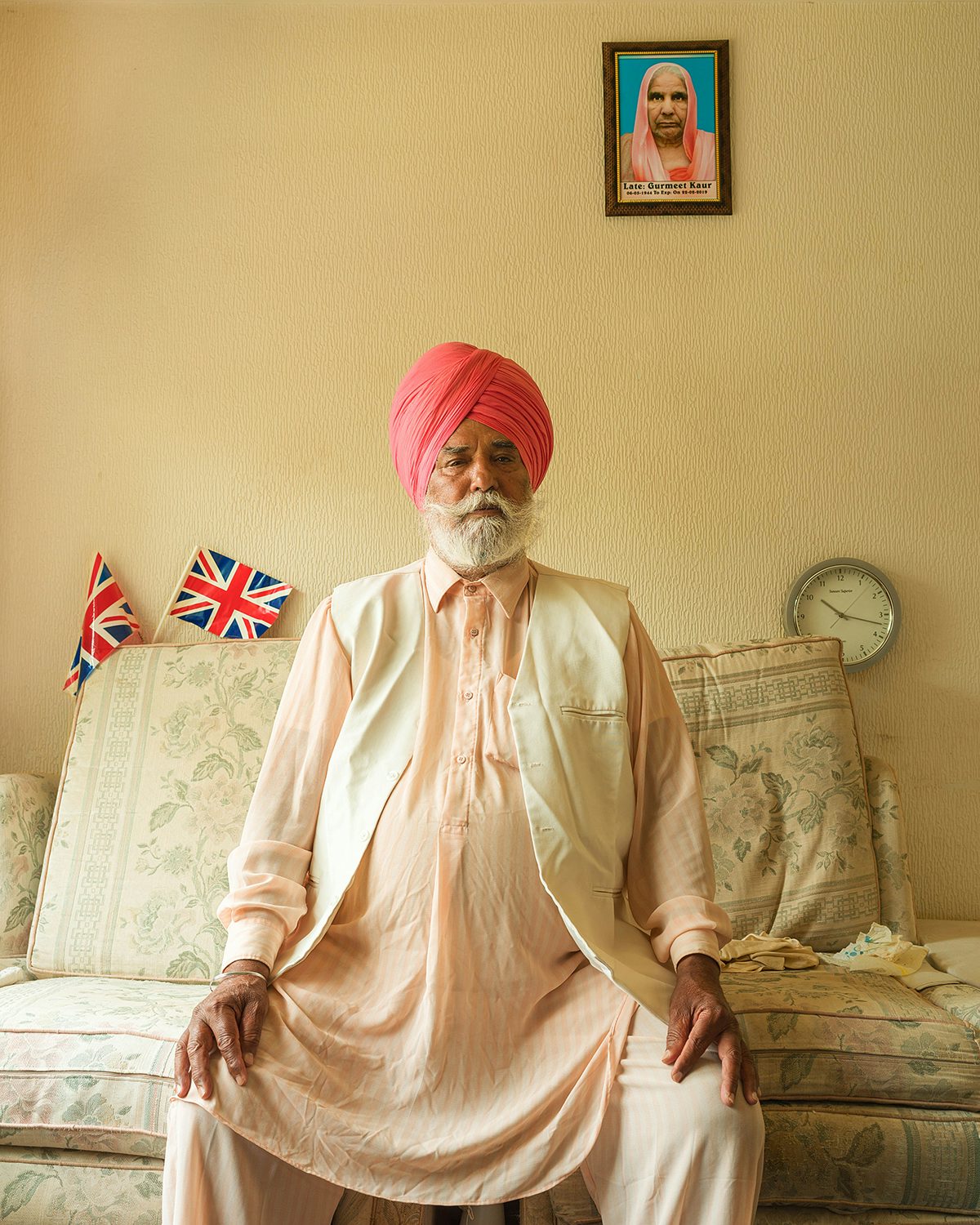 Image shows a man sat on a sofa with union jacks in the background, taken from Kavi Pujara's book This Golden Mile