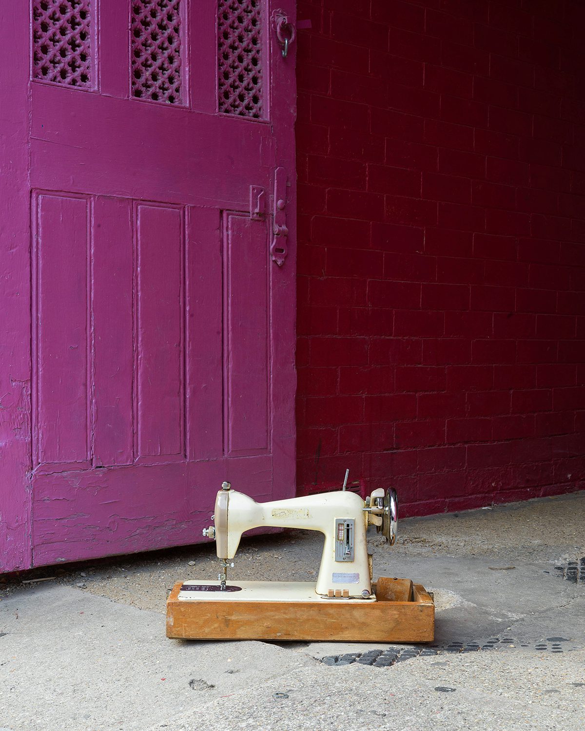 Image shows a sewing machine on the floor next to a purple door, taken from Kavi Pujara's book This Golden Mile
