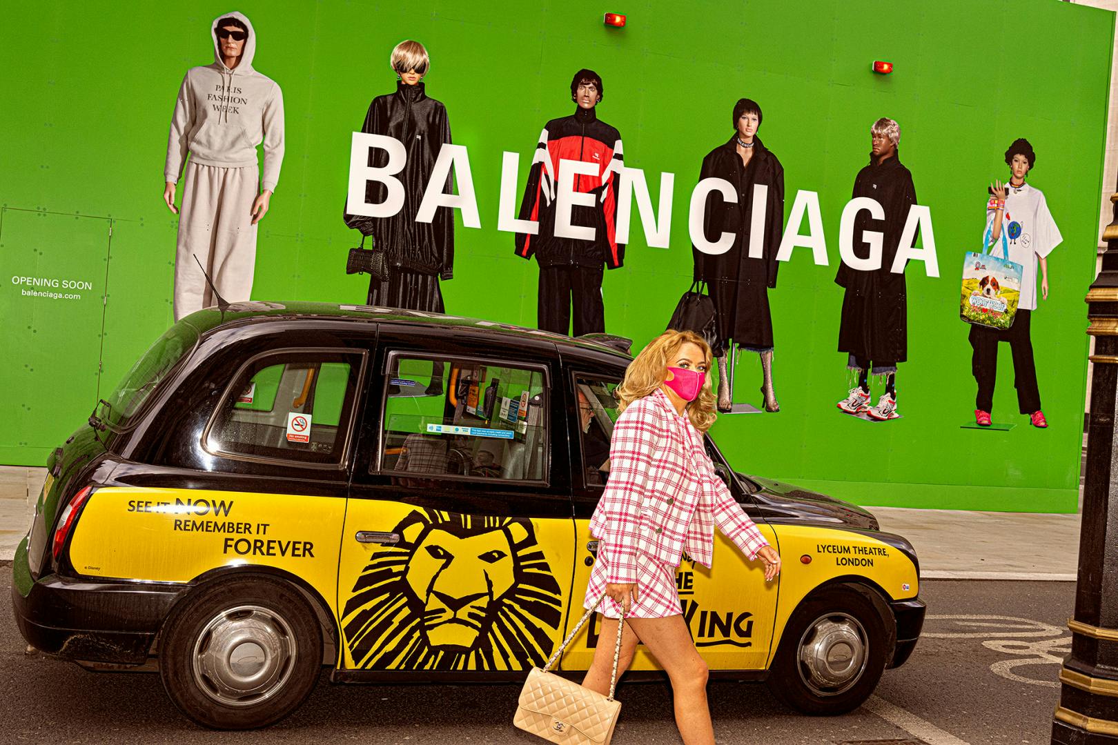 Photograph of a person in a pink skirt suit and a Covid-19 mask, walking past a taxi and a Balenciaga sign, in Soho Unlocked by Dougie Wallace