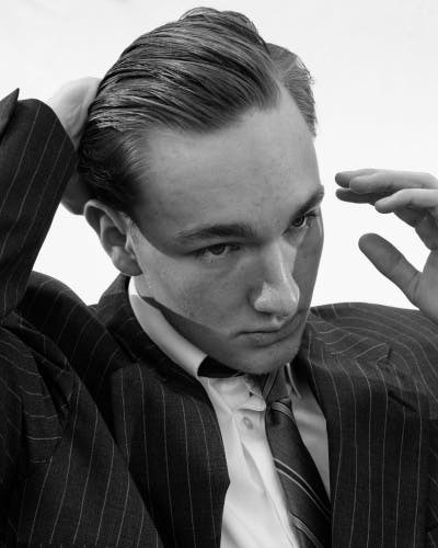 Black and white portrait of a person wearing a suit sweeping their hair back, in the Four Pillars book by Eli Durst