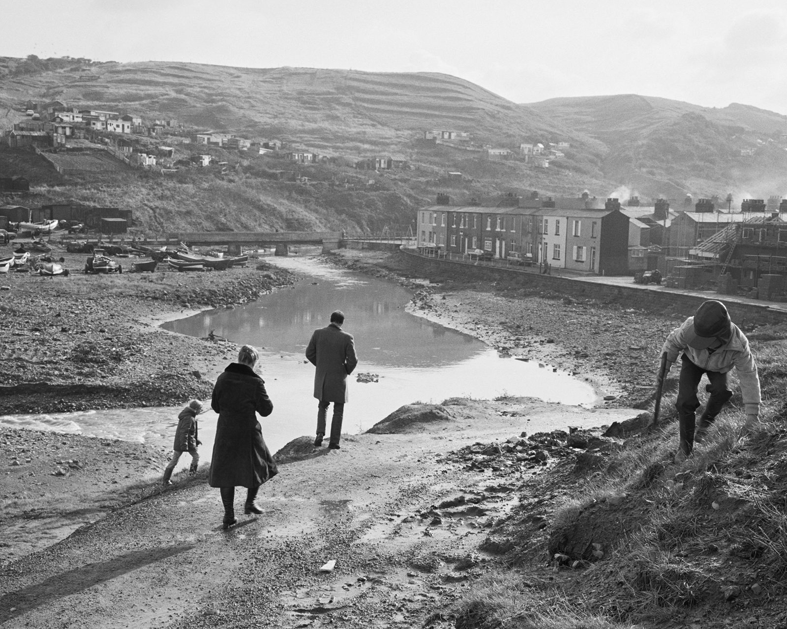 Black and white image shows a family of four walking along the banks of a river, which appears in the new Chris Killip exhibition
