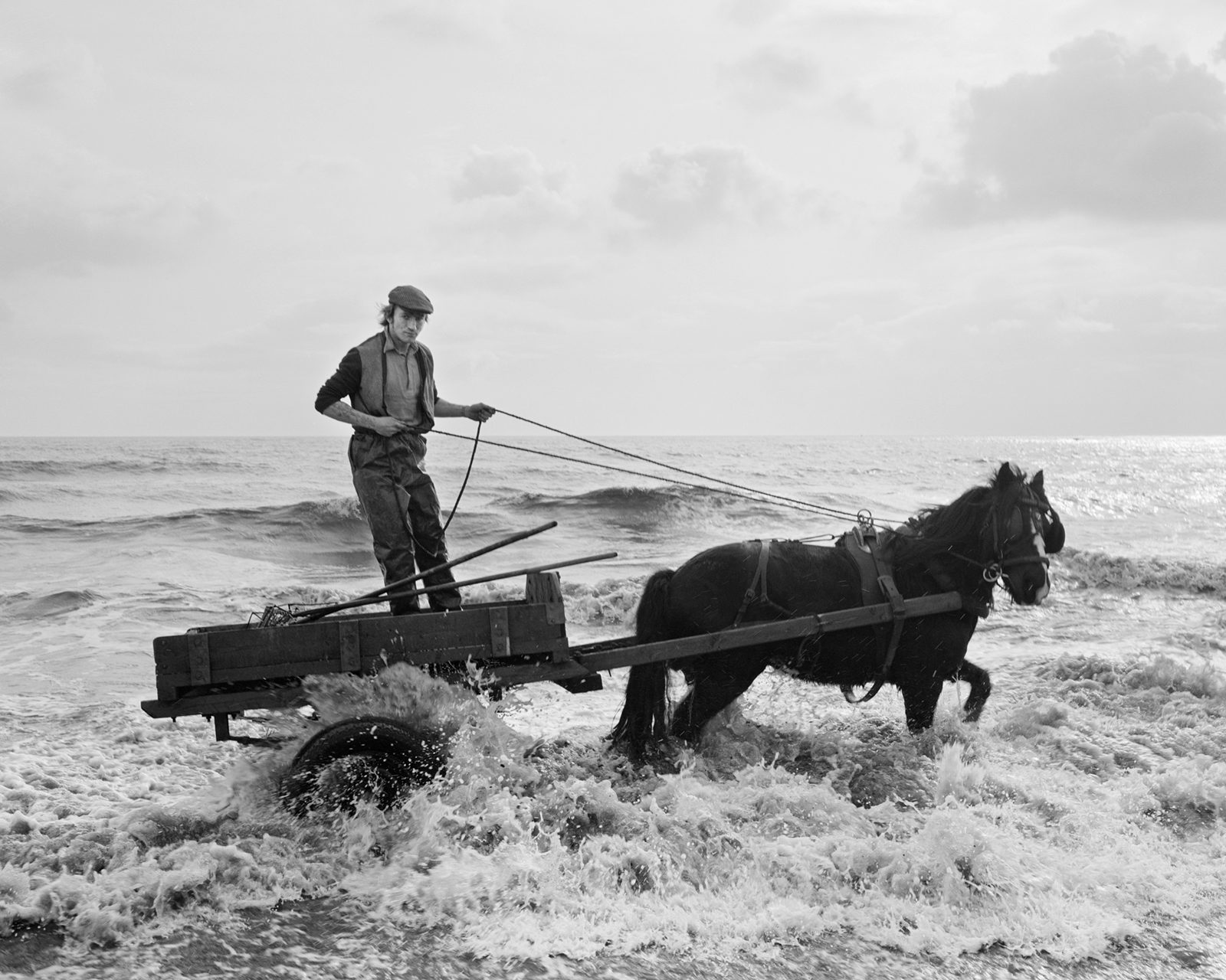 Black and white image of a person steering a horse and cart in the sea, which appears in the new Chris Killip exhibition
