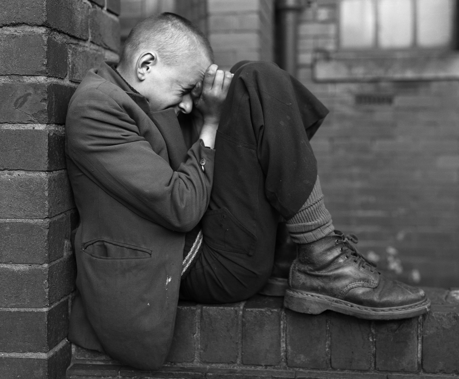 Black and white side-on photograph of a young person hunched up on a wall with a pained expression, which appears in the new Chris Killip exhibition