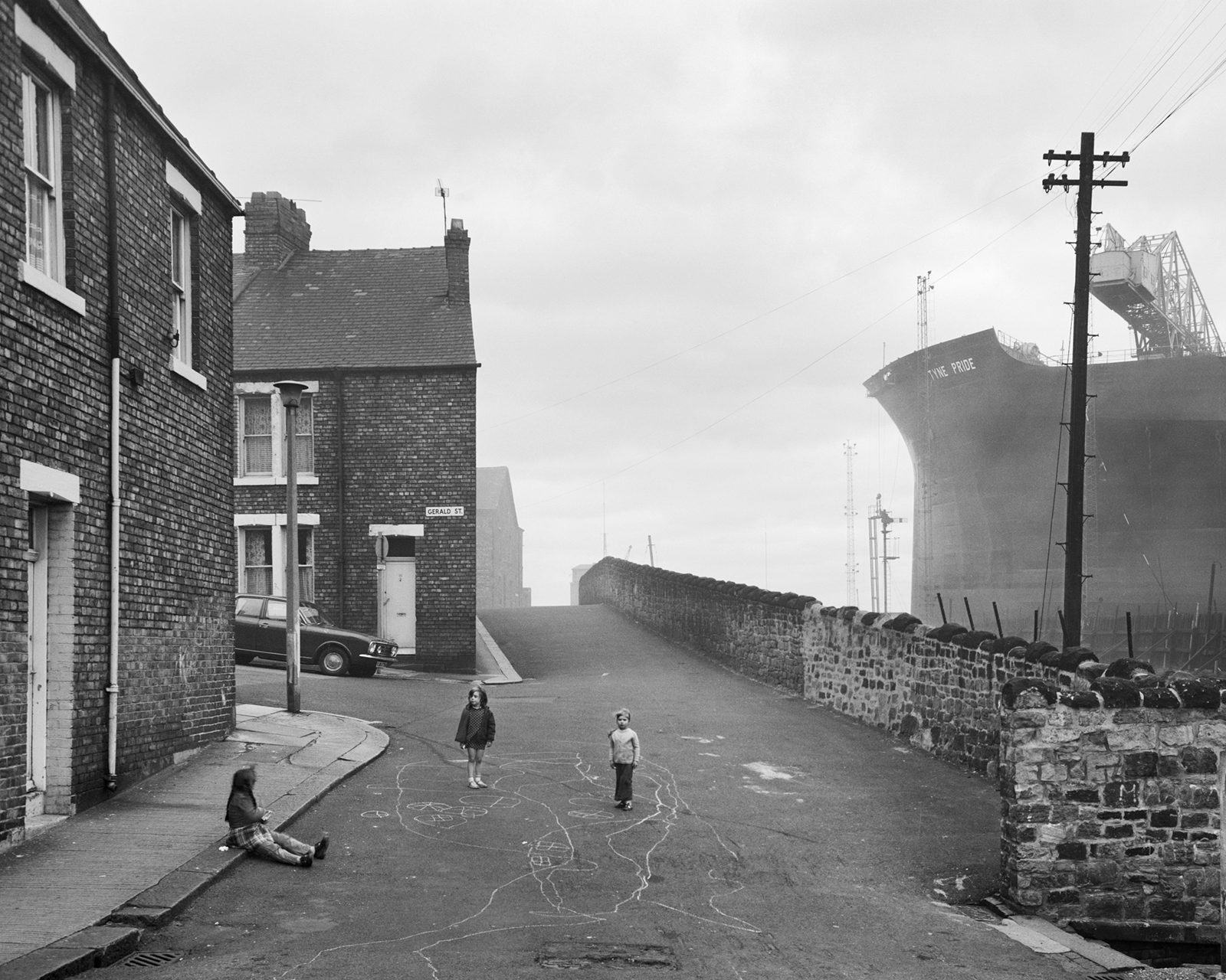 Black and white photograph of three children in the street with a ship docked next to it, which appears in the new Chris Killip exhibition