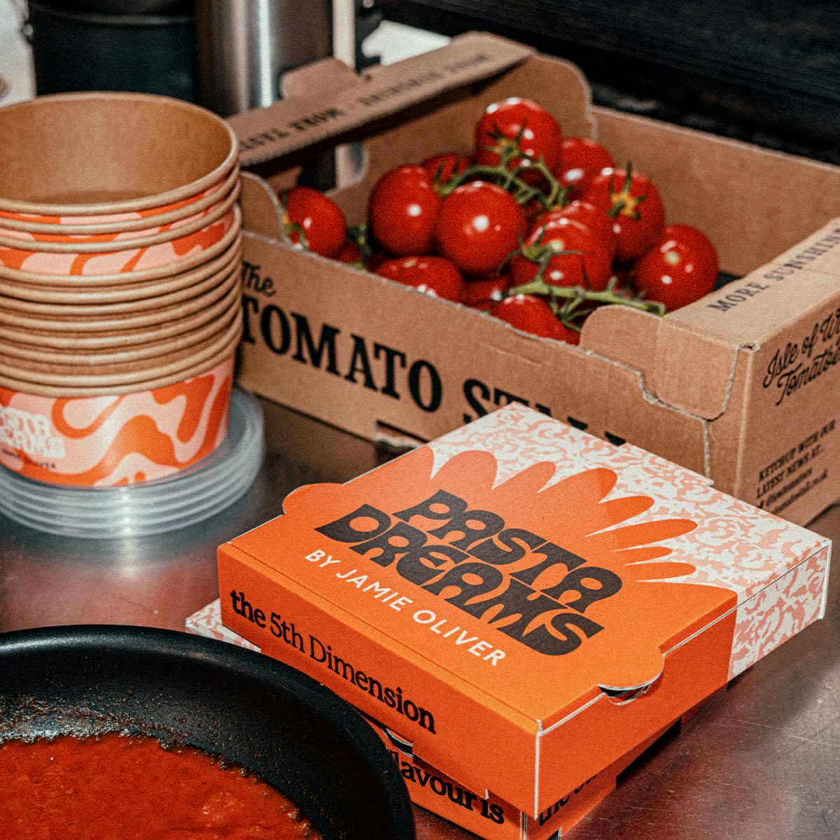 Image shows a packaging box labelled 'Pasta Dreams' next to a crate of tomatoes