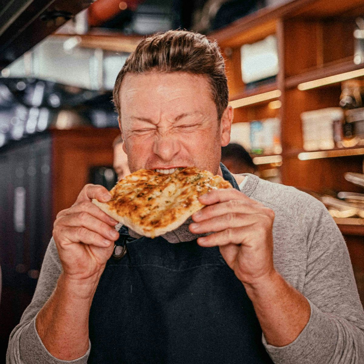 Image shows Jamie Oliver biting into food
