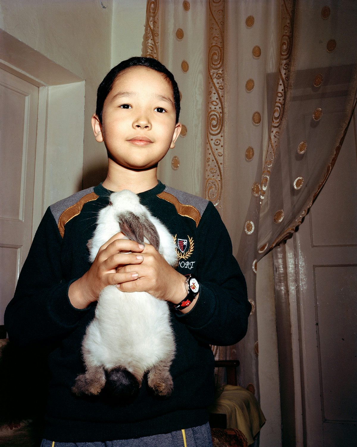 Image shows a young boy holding a rabbit to his chest, photographed by Taylor Wessing portrait prize runner-up, Alexander Komenda