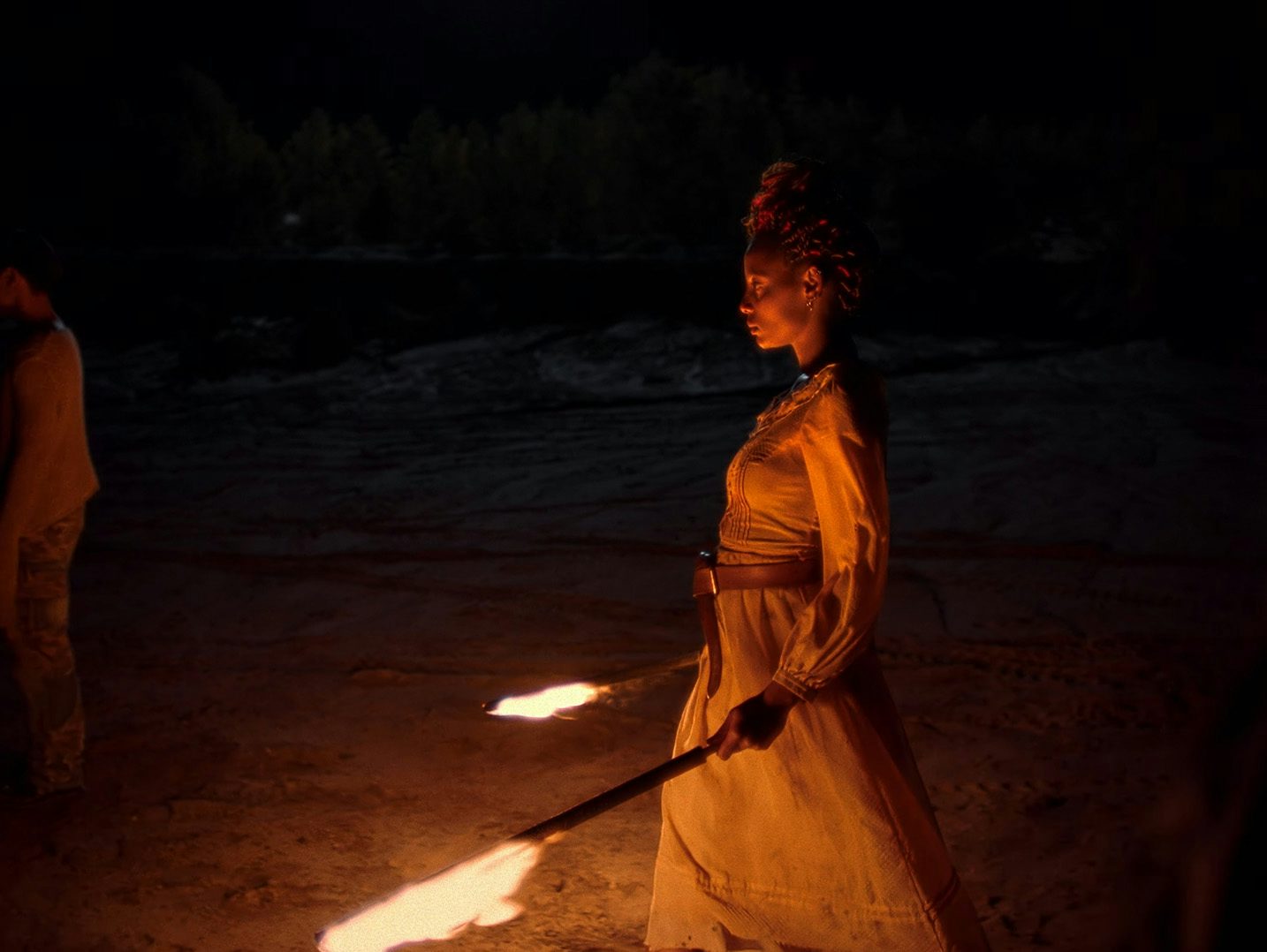 Image shows a person carrying two batons on fire in the music video for I Saw by Young Fathers