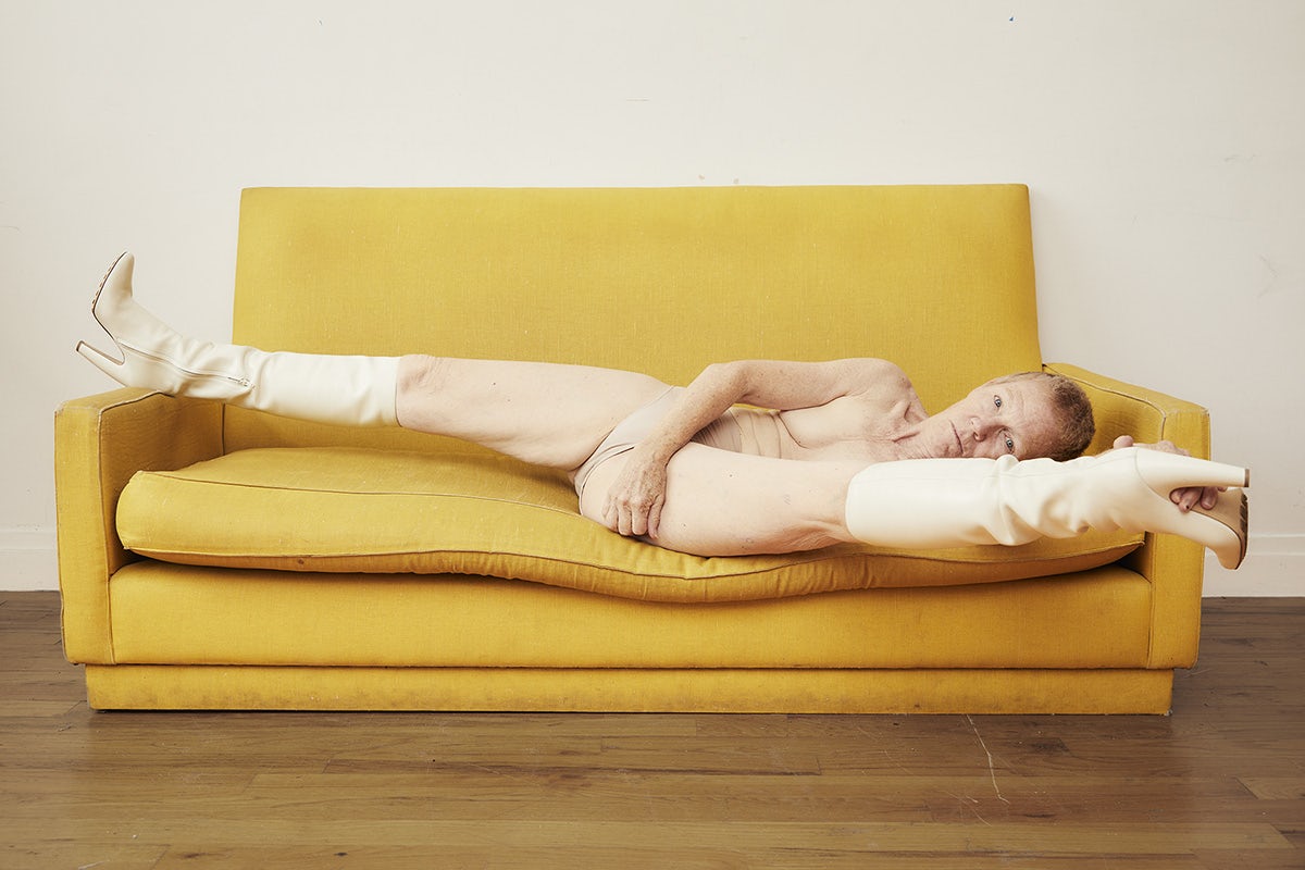 Image by Charlie Engman for SZ Magazin of his mother lying down doing the splits on a yellow sofa, while wearing cream thigh boots