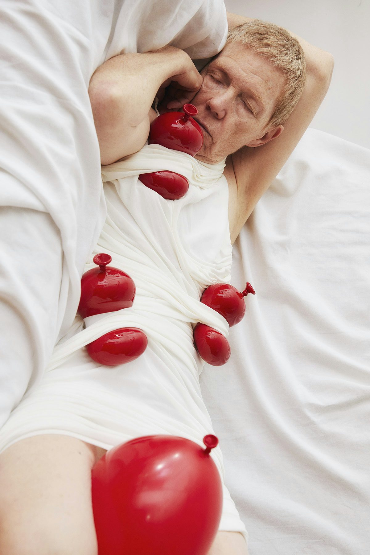 Image by Charlie Engman for SZ Magazin of his mother lying down. She wears a white dress with other red balloons strapped to her