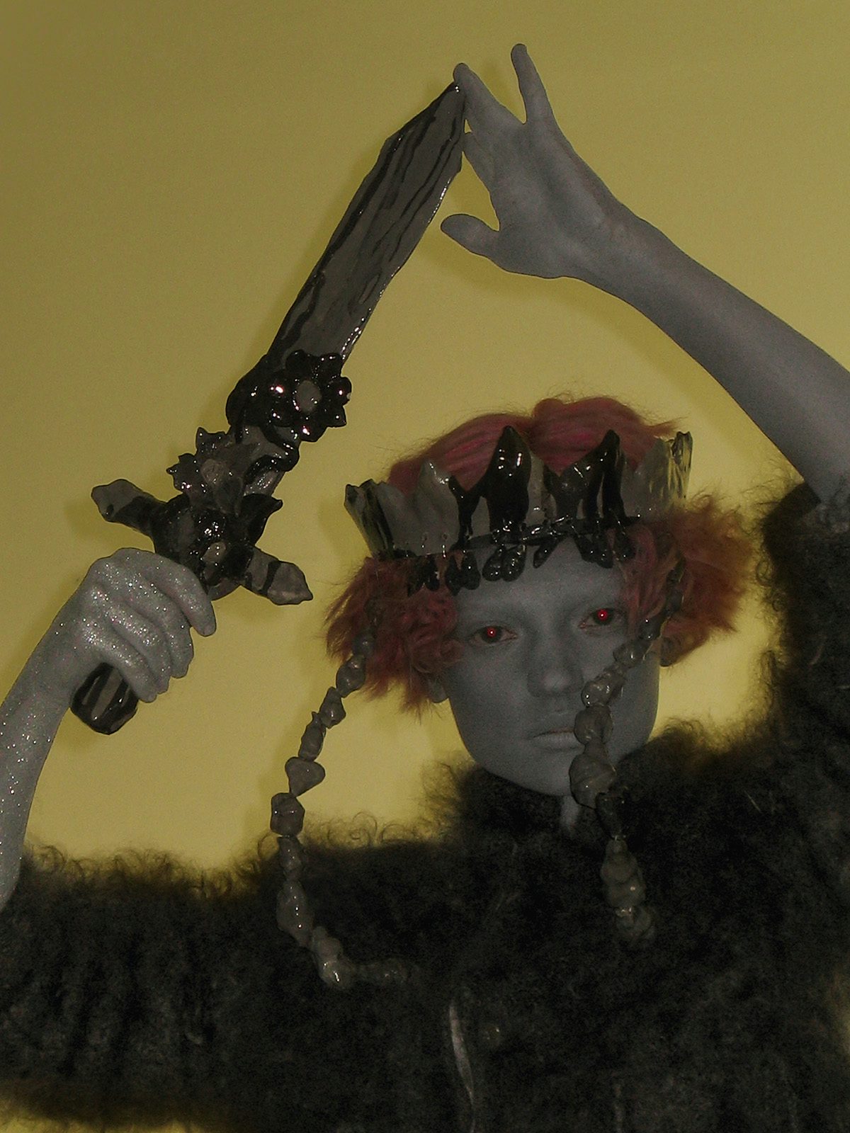 Image by Harley Weir of a person with green shimmering holding a sword above their head and wearing a fluffy garment and a headpiece