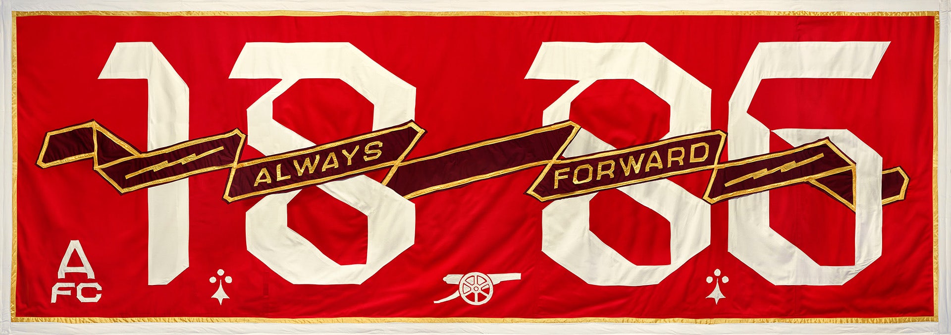 Image shows a red Arsenal banner by Jeremy Deller with the date 1886 in white angular lettering, and a scroll running through the middle of the image which reads 'Always Forward'