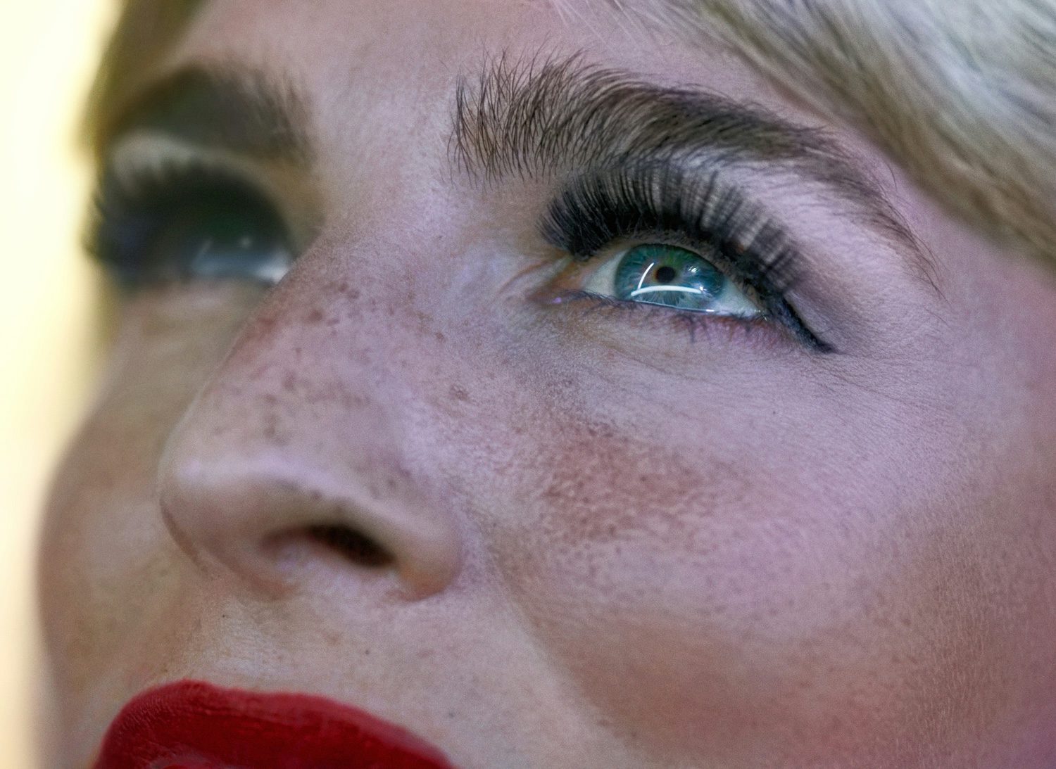 Image by Alex Prager shows a close crop photograph of a person's face wearing red lipstick and gazing upwards