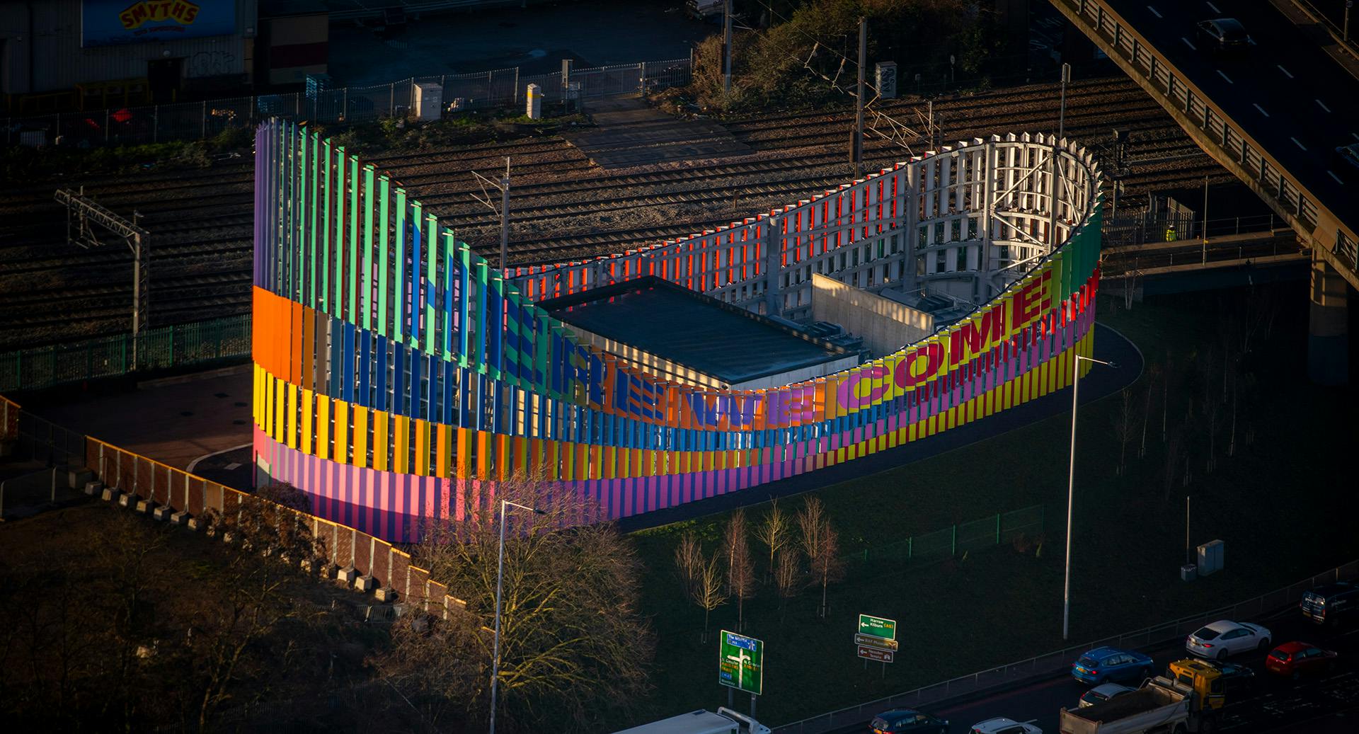 Image shows the colourful exterior of the Brent Cross Town electrical substation next to a busy road, designed by artist Lakwena