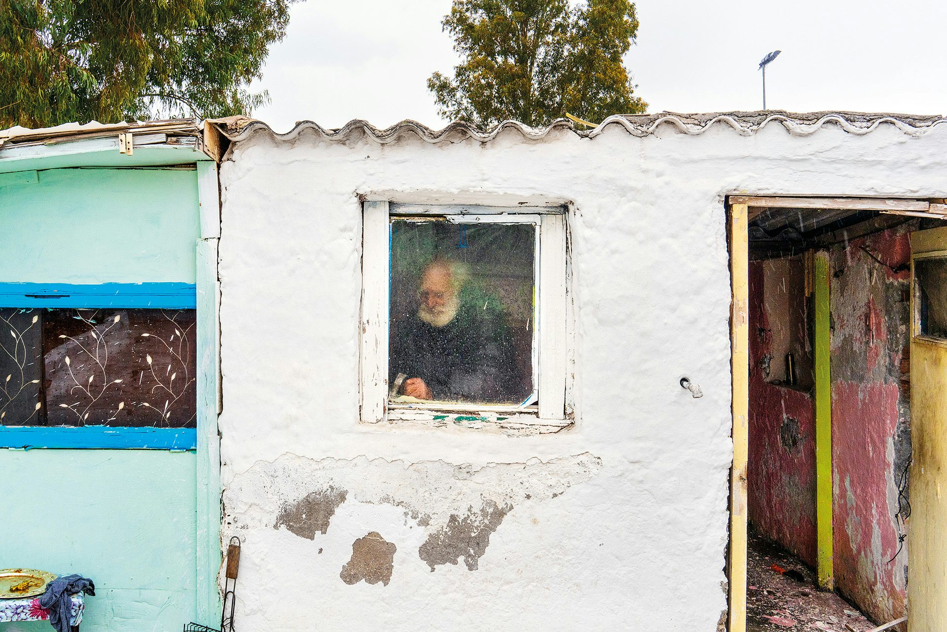 Image by Niko J. Kallianiotis shows a person inside a small white building framed by the window