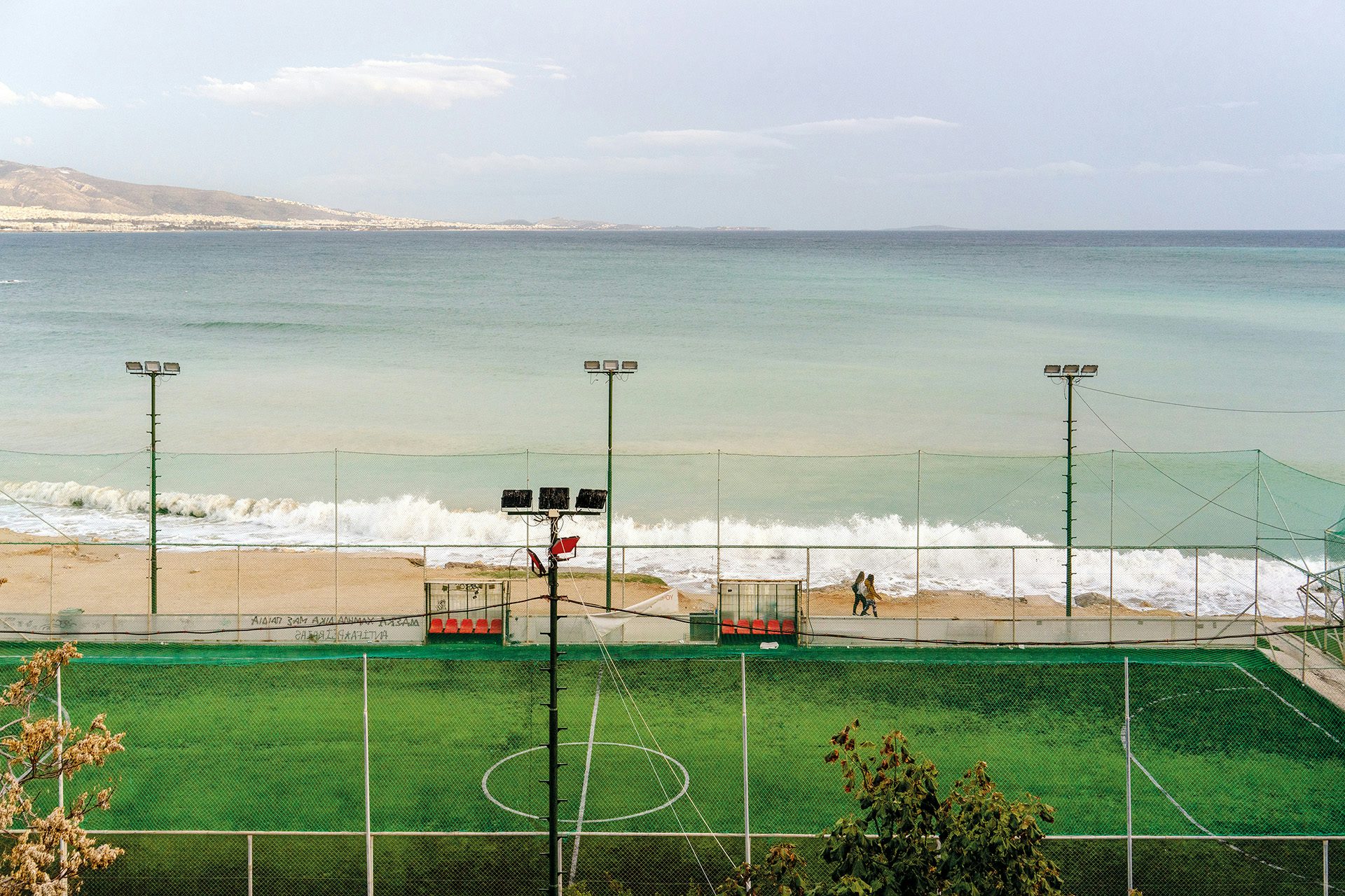 Image by Niko J. Kallianiotis shows a grassy sports field overlooking the coastline of Athens