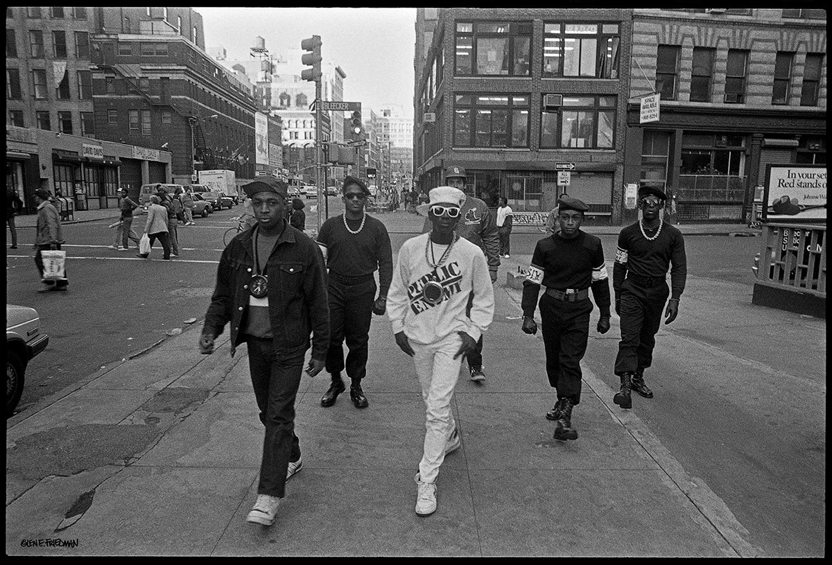 Black and white photograh of hip hop group Public Enemy walking in a line through a New York City street