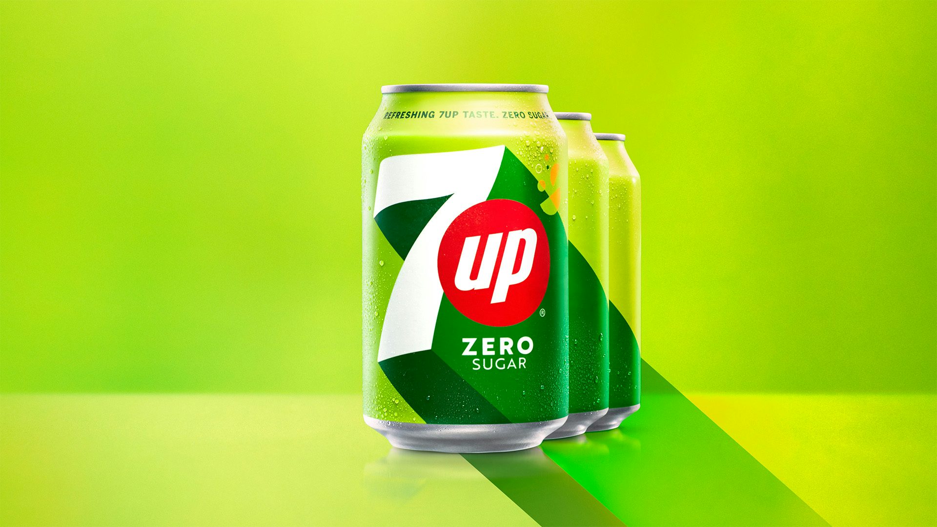Image shows three cans of 7UP in a row, featuring its new green and lime packaging design