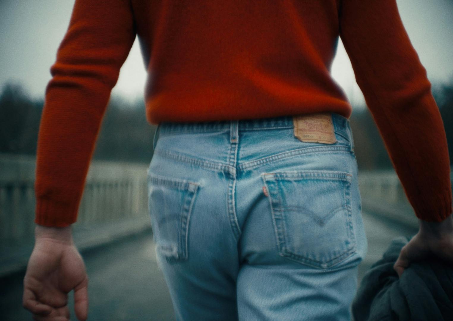 Image shows a person from behind wearing a pale blue pair of Levis 501 jeans and a red sweater