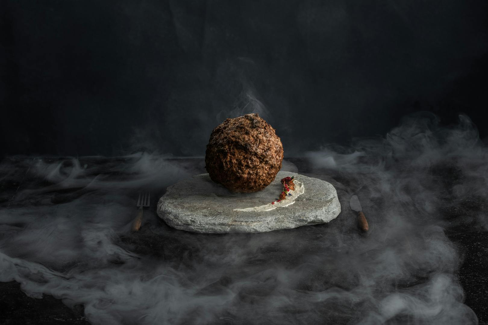 Image of the mammoth meatball shown on a stone serving plate surrounded by smoke