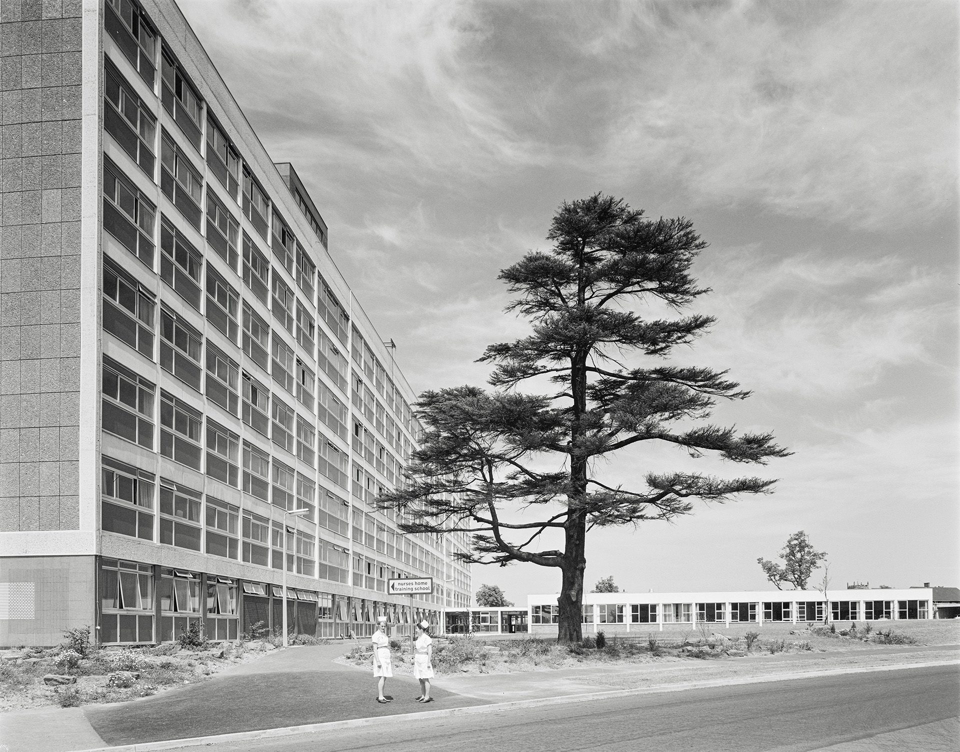 Black and white photograph of a large brutalist hospital building with a tree in front of it
