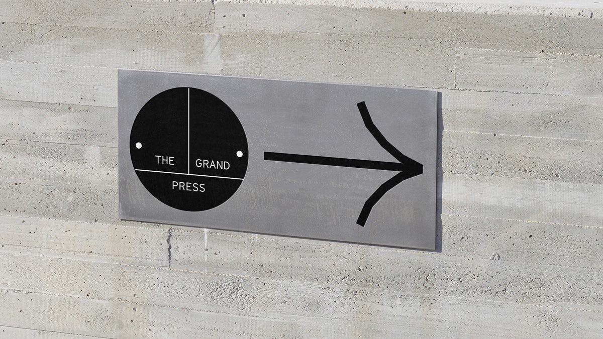 Image shows a steel sign with the Grand Press logo and an arrow pointing to the right