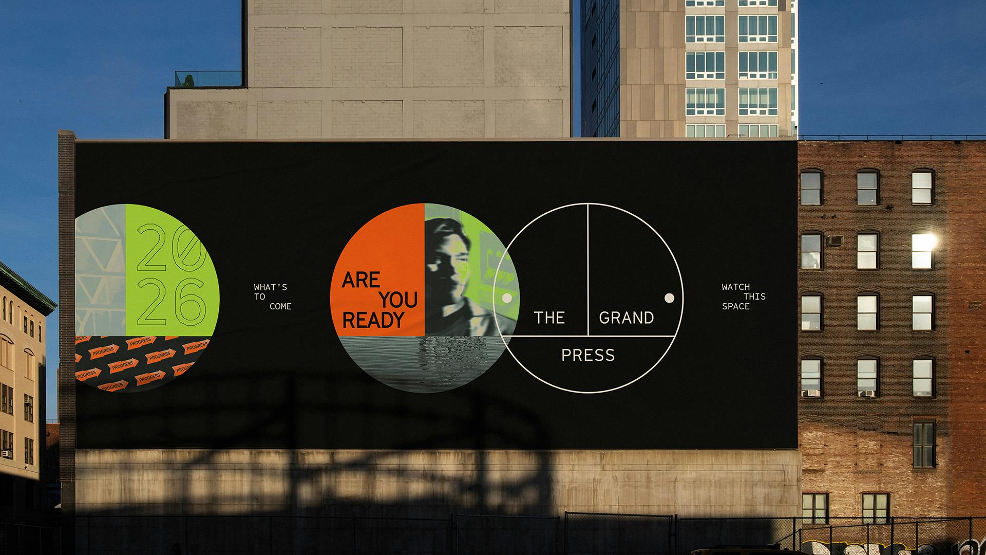 Image shows posters for the Grand Press attached to the side of a building. The posters feature the circular Grand Press logo, and another circular shape with the phrase 'Are you ready?' on the left