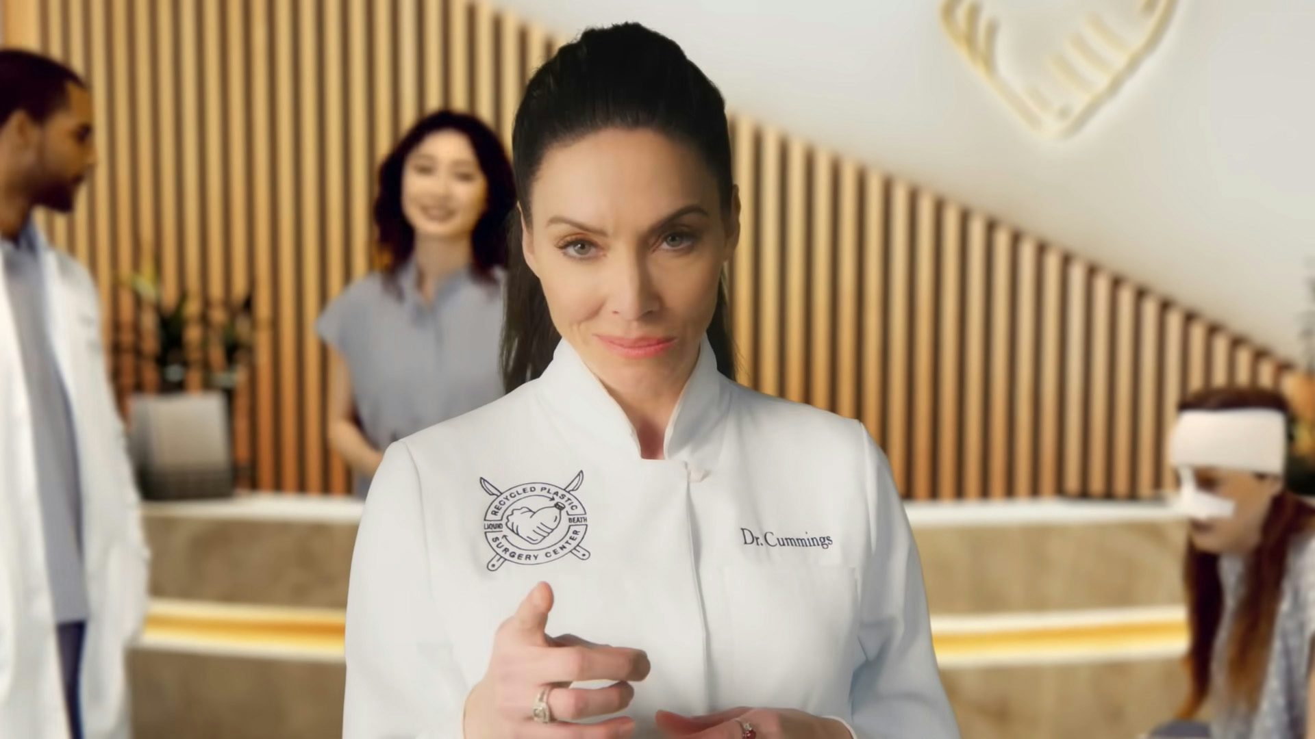Still from Liquid Death's spoof advert showing actor Whitney Cummings in the role of a surgery saleswoman, wearing a white lab coat and pointing at the camera with a smile,