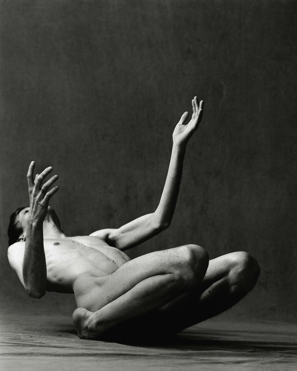 Black and white photograph from O by Luis Alberto Rodriguez, showing a person crouching on the ground leaning backwards with their arms raised in the air