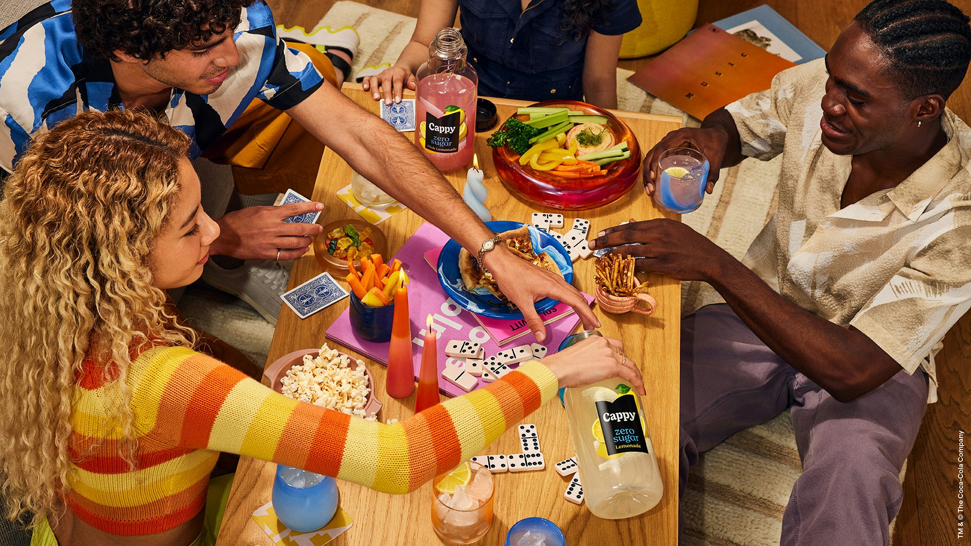 Image shot as part of Minute Maid's new branding showing people sat around a table covered in dominoes, popcorn, and Minute Maid drinks