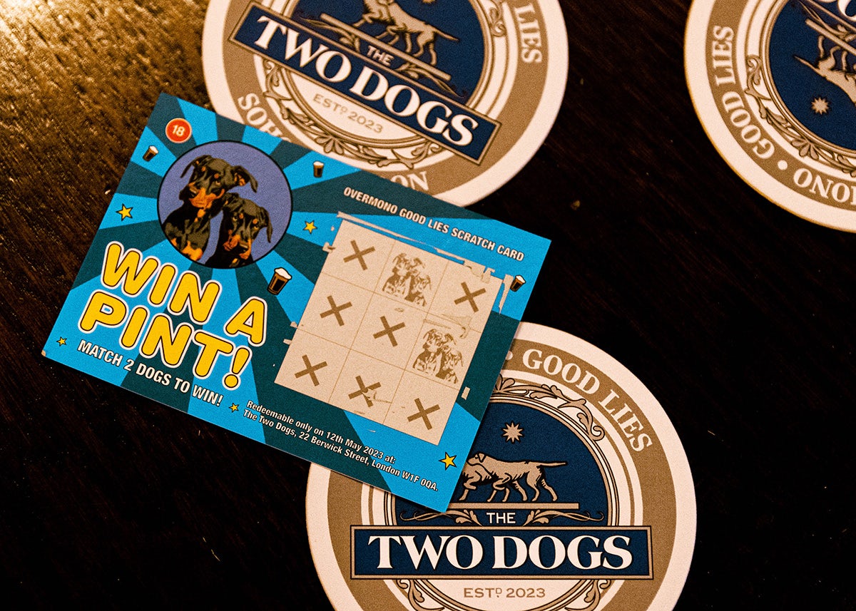 Image shows a coaster for Overmono's Two Dogs pop-up featuring ornate border designs and a regal portrait of two Dobermann dogs, and a special scratchcard labelled 'win a pint' and an illustration of the two dogs