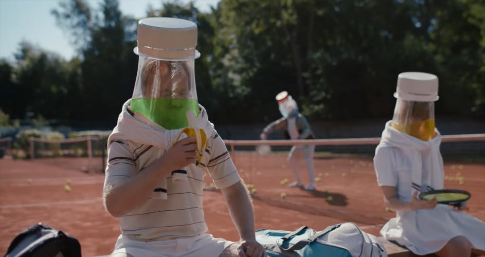 Still image from Waterdrop's advert, showing two people sat down, who have drinks bottles for heads and are wearing tennis kits. One is trying to eat a banana through the plastic bottle covering their head. A third person with a bottle for a head is playing tennis on a red tennis court in the background