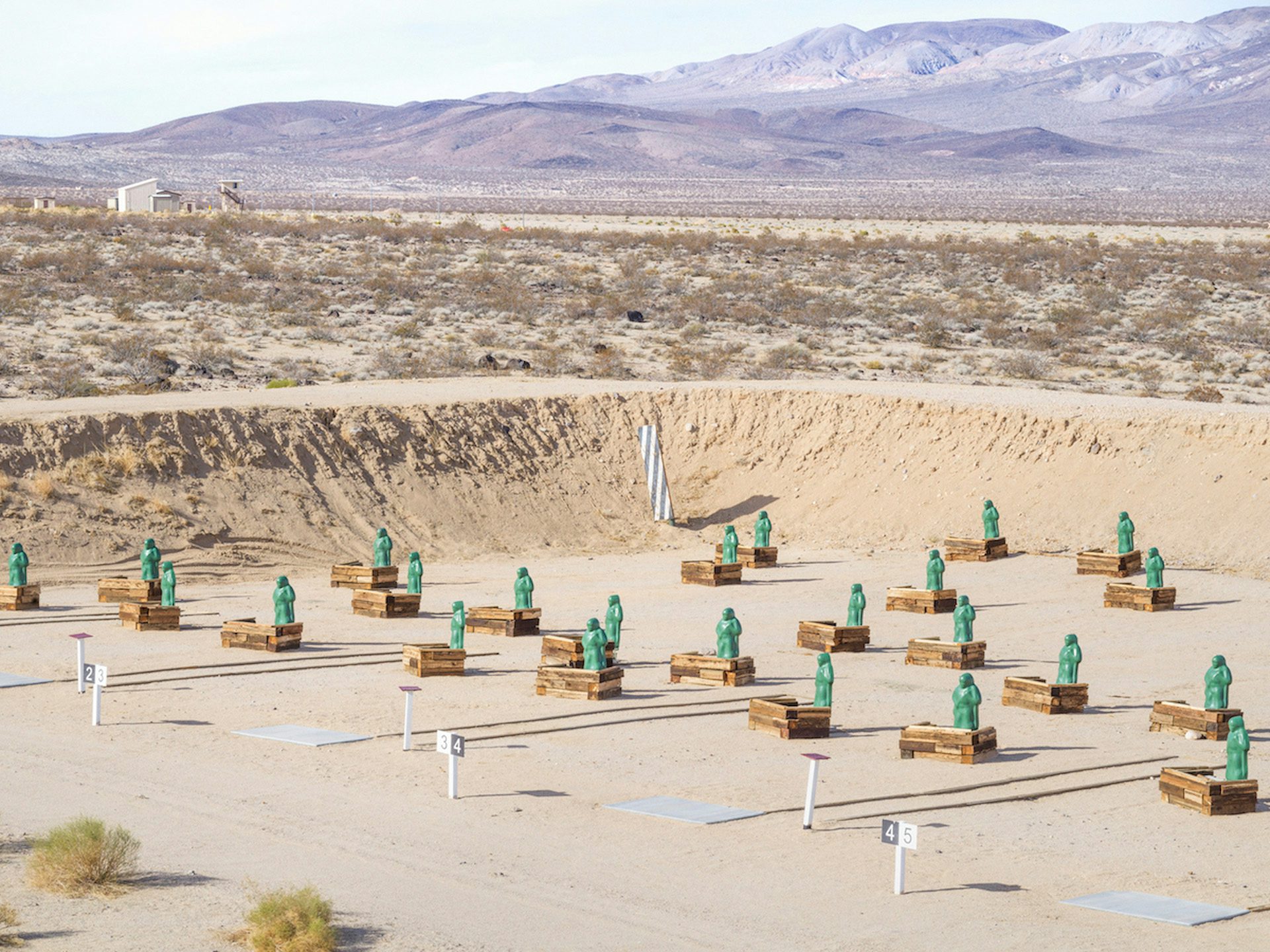 Image from American Glitch by Andrea Orejarena and Caleb Stein showing a series of green figures arranged in a desert firing range
