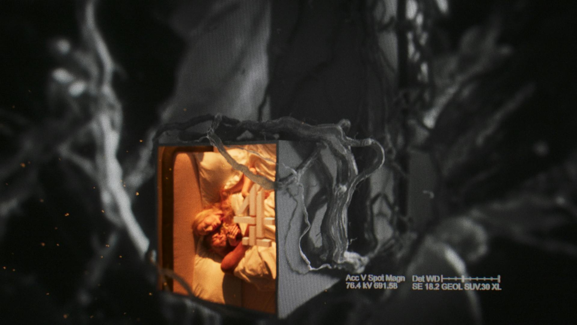 Still image from the new Channel 4 idents showing two people embracing on a bed, shown via a cube shaped portal encased in the Channel 4 logo