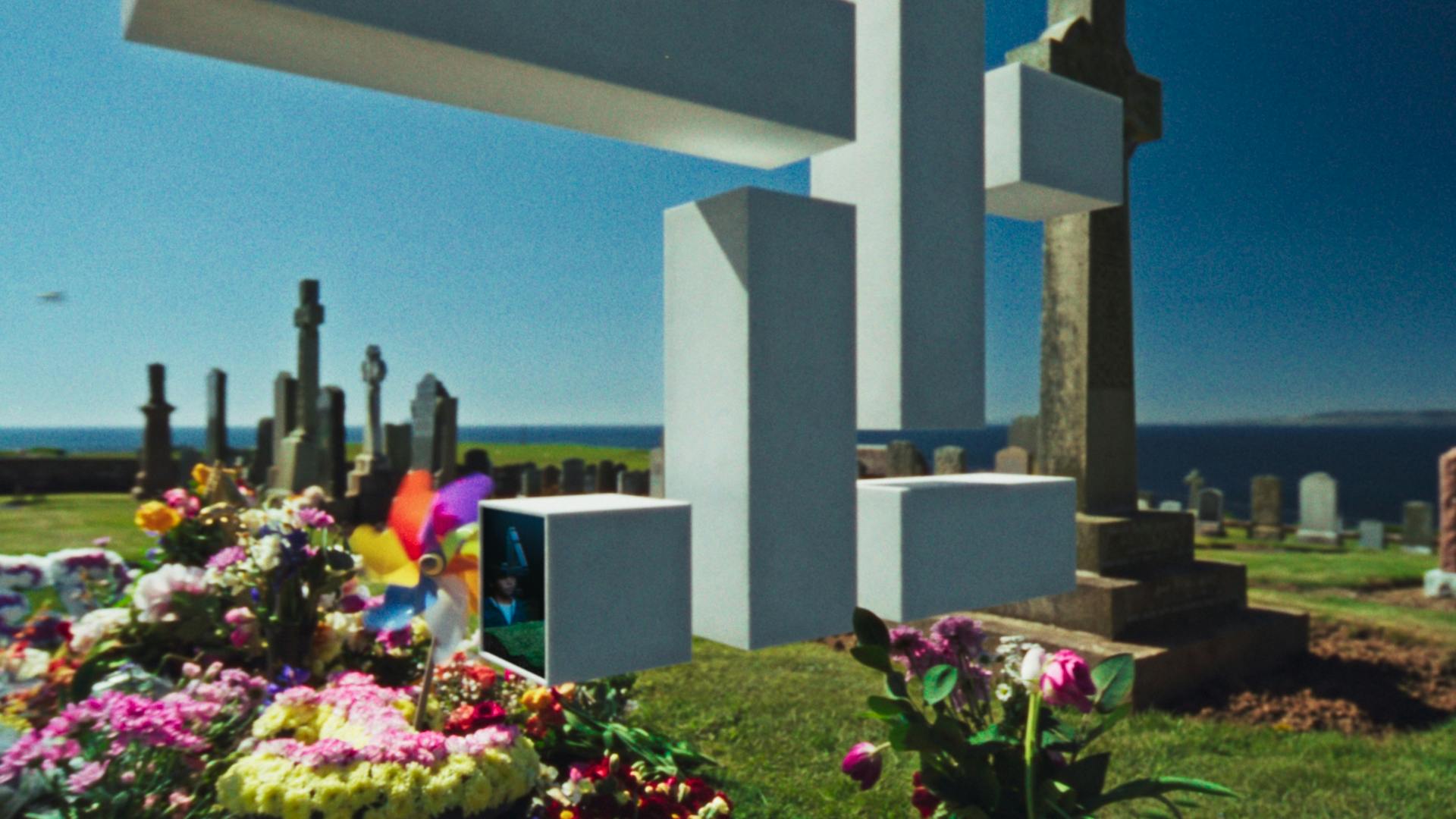 Still image from the new Channel 4 idents showing the 4 logo in 3D, floating above a graveyard filled with flowers by the coast