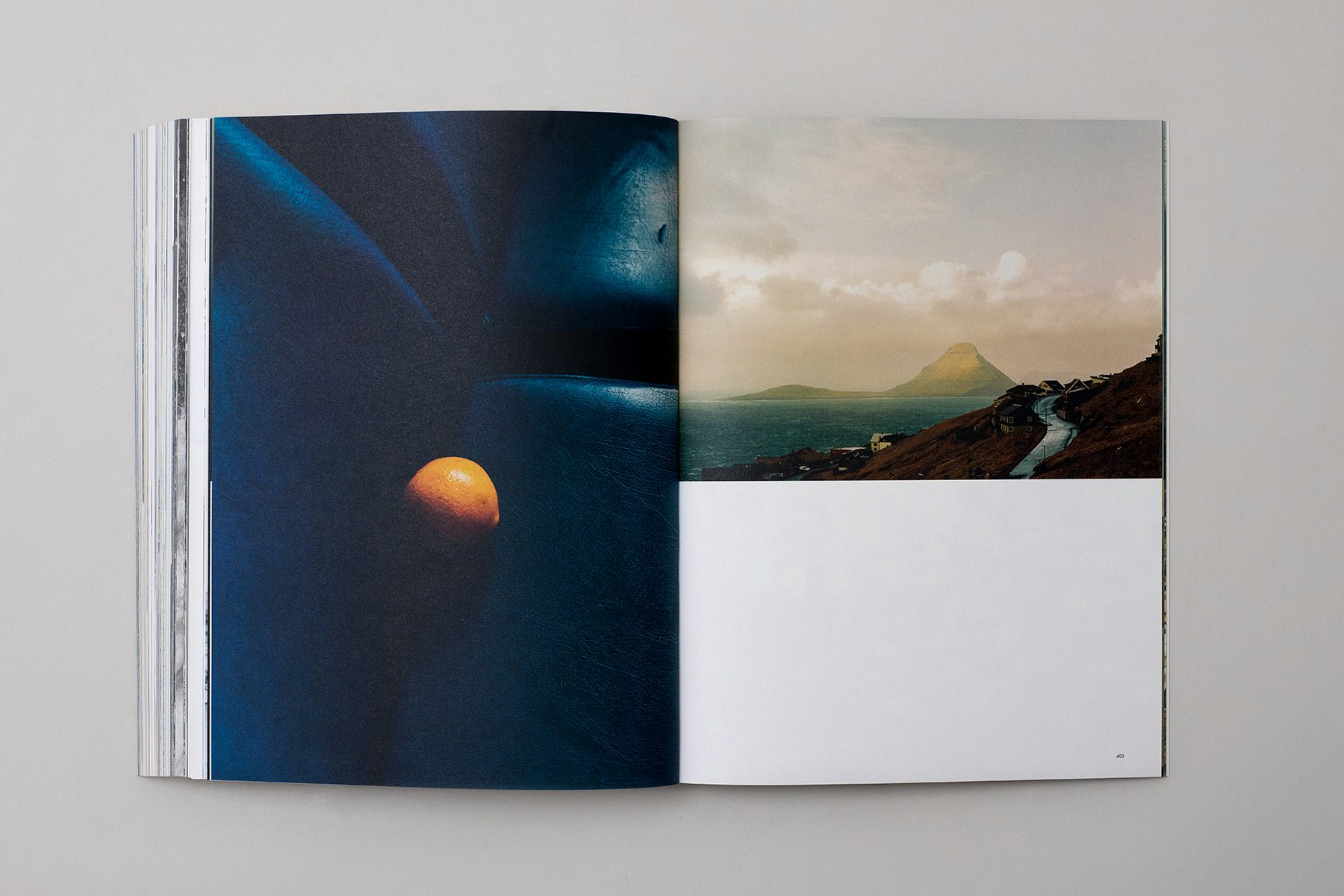 Photograph of a spread from the Blue issue of The Colour Journal, showing a photo of an orange on a dark blue leathery surface on the left hand page, and a landscape half-page photograph of a hillside road and a mountain in the background